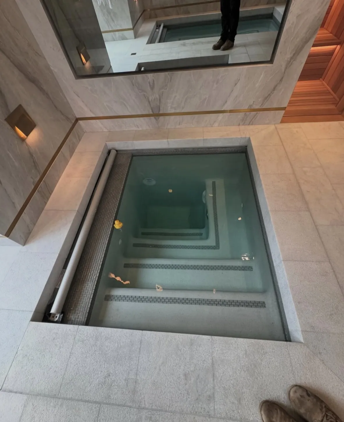Square indoor spa with light stone surround, internal steps with dark tile bands, and a retractable cover roller.