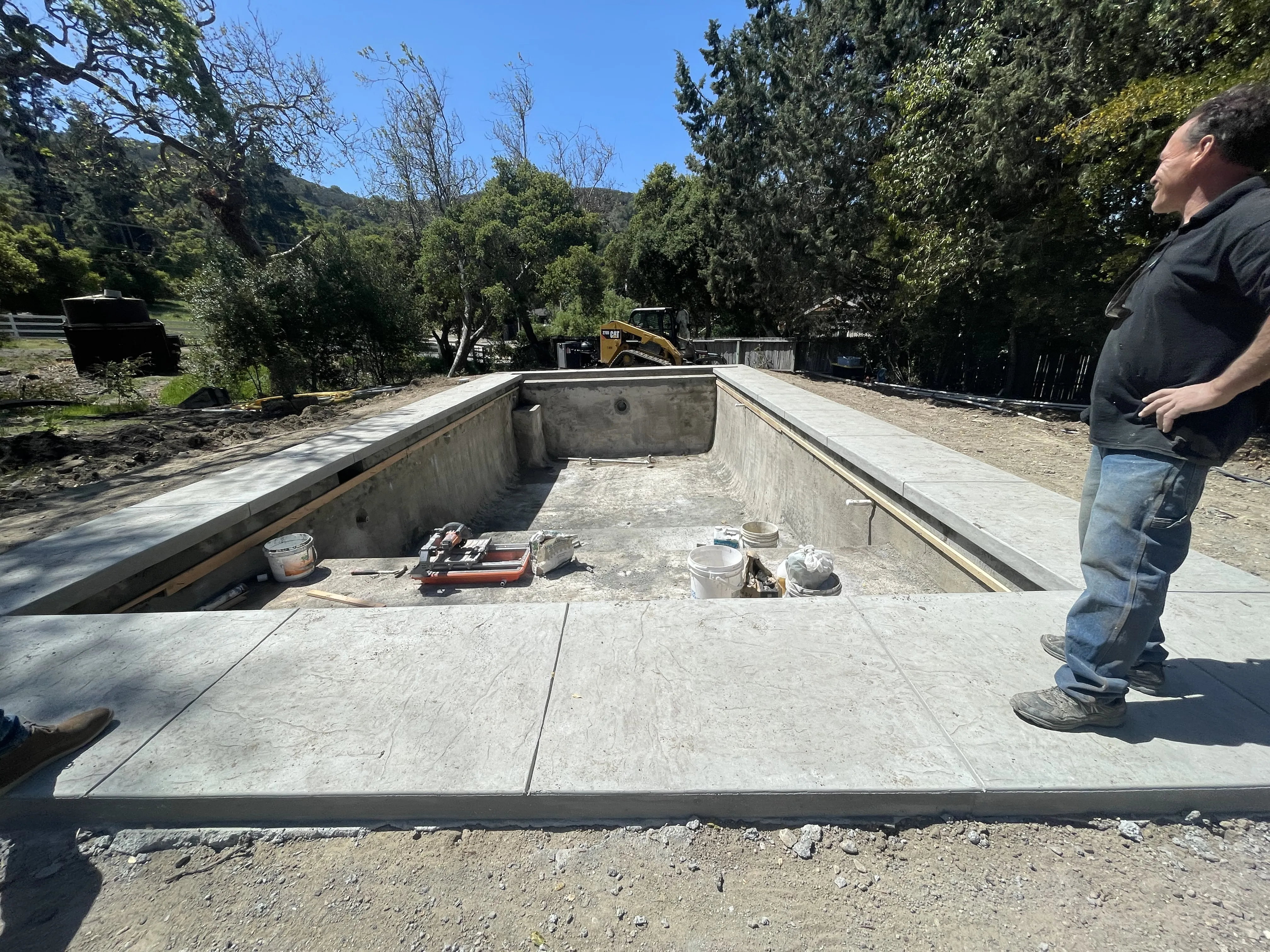 Upside down view of a rectangular pool shell under construction with newly poured concrete decking and wooden forms.