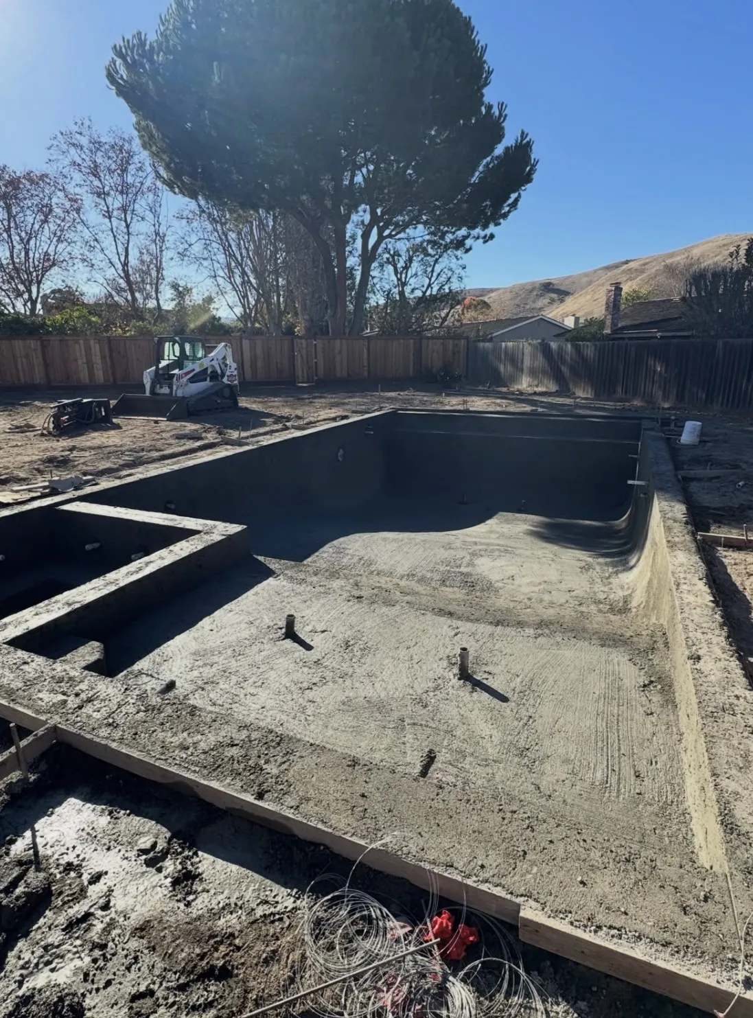 Rough concrete pool shell with a baja shelf, integrated spa, and PVC stub-outs during construction.