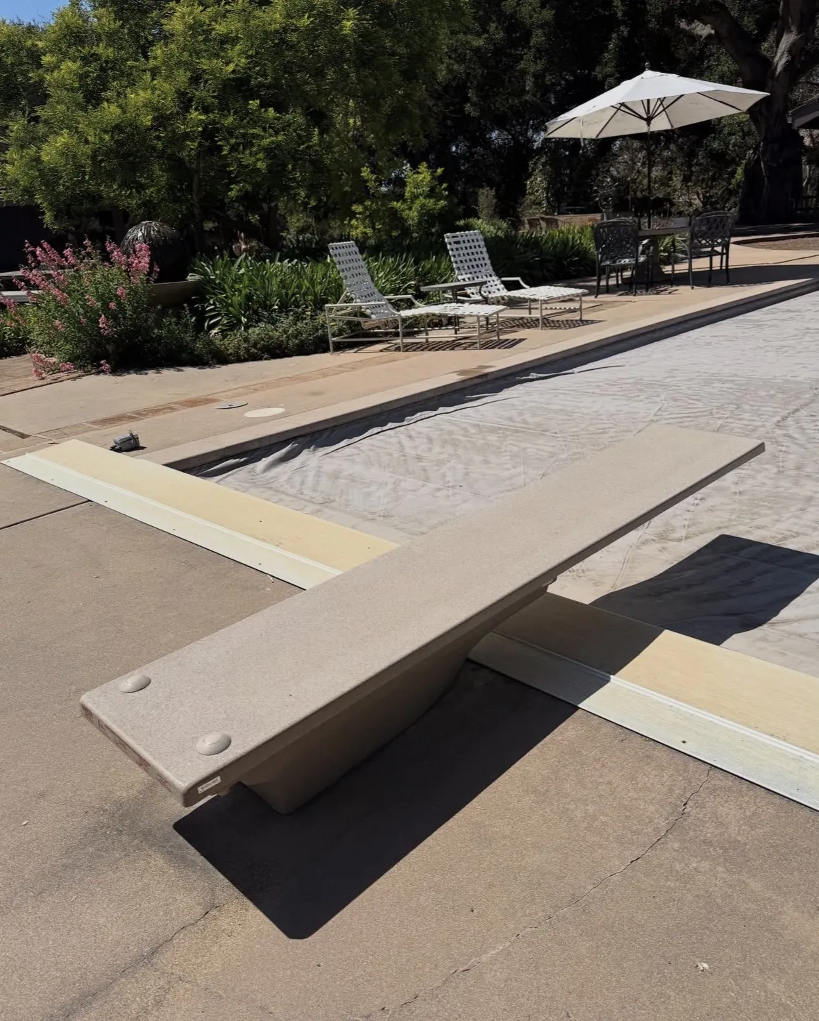 Covered swimming pool featuring a tan diving board on a concrete deck.