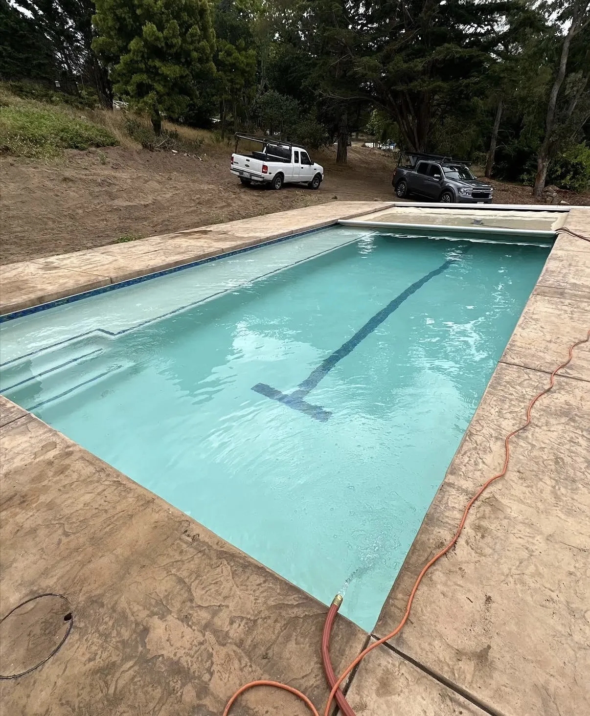 Rectangular lap pool with a blue racing lane line and automatic cover being filled with a hose.