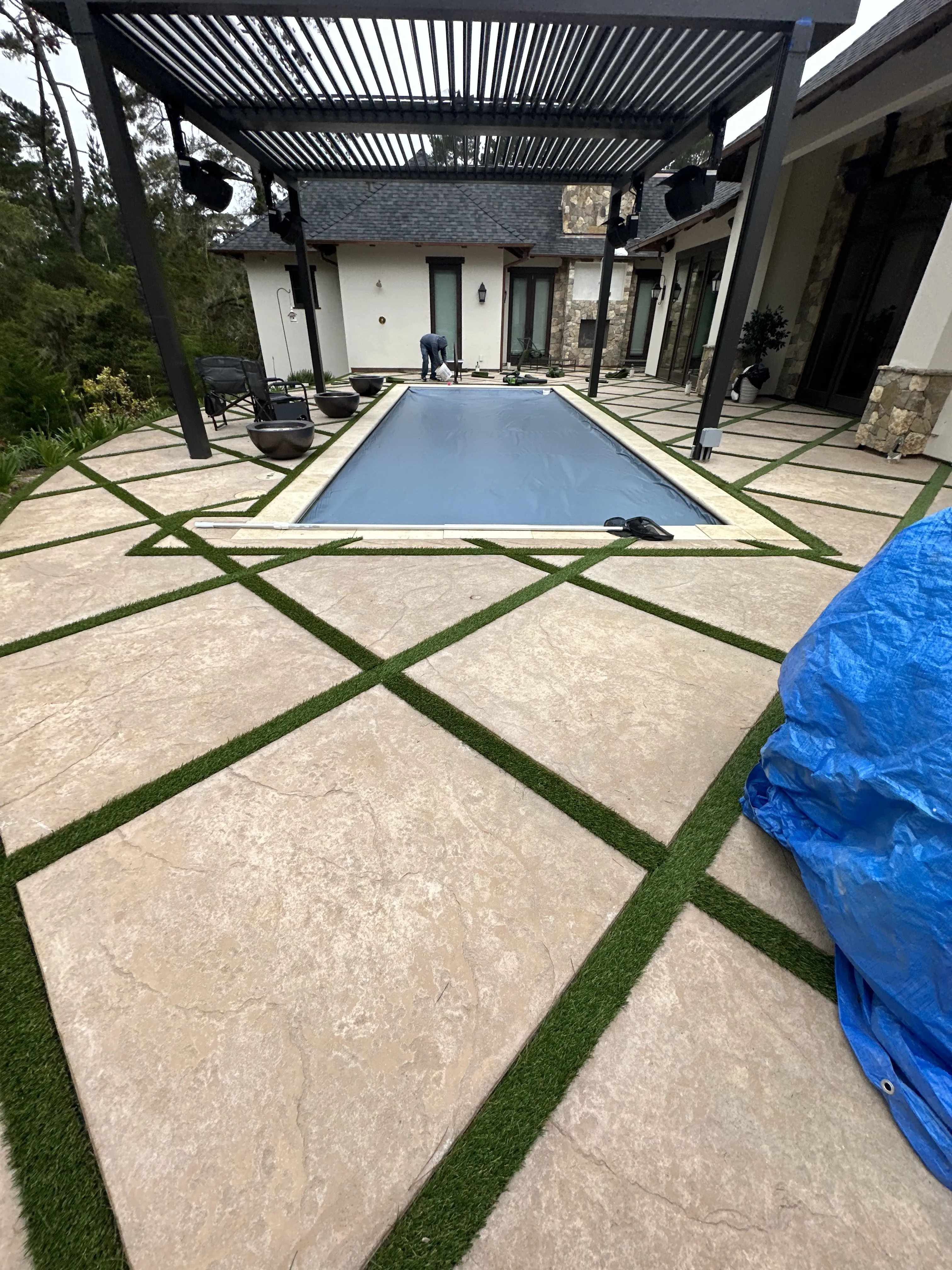 Rectangular pool with closed cover surrounded by stone pavers and artificial turf in a backyard.
