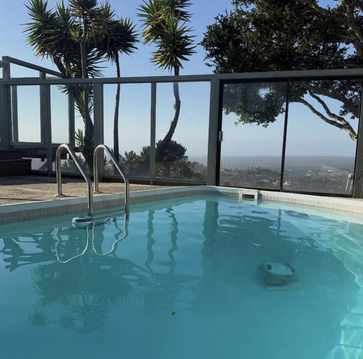 A swimming pool with a metal ladder and framed glass fence overlooking a panoramic view.