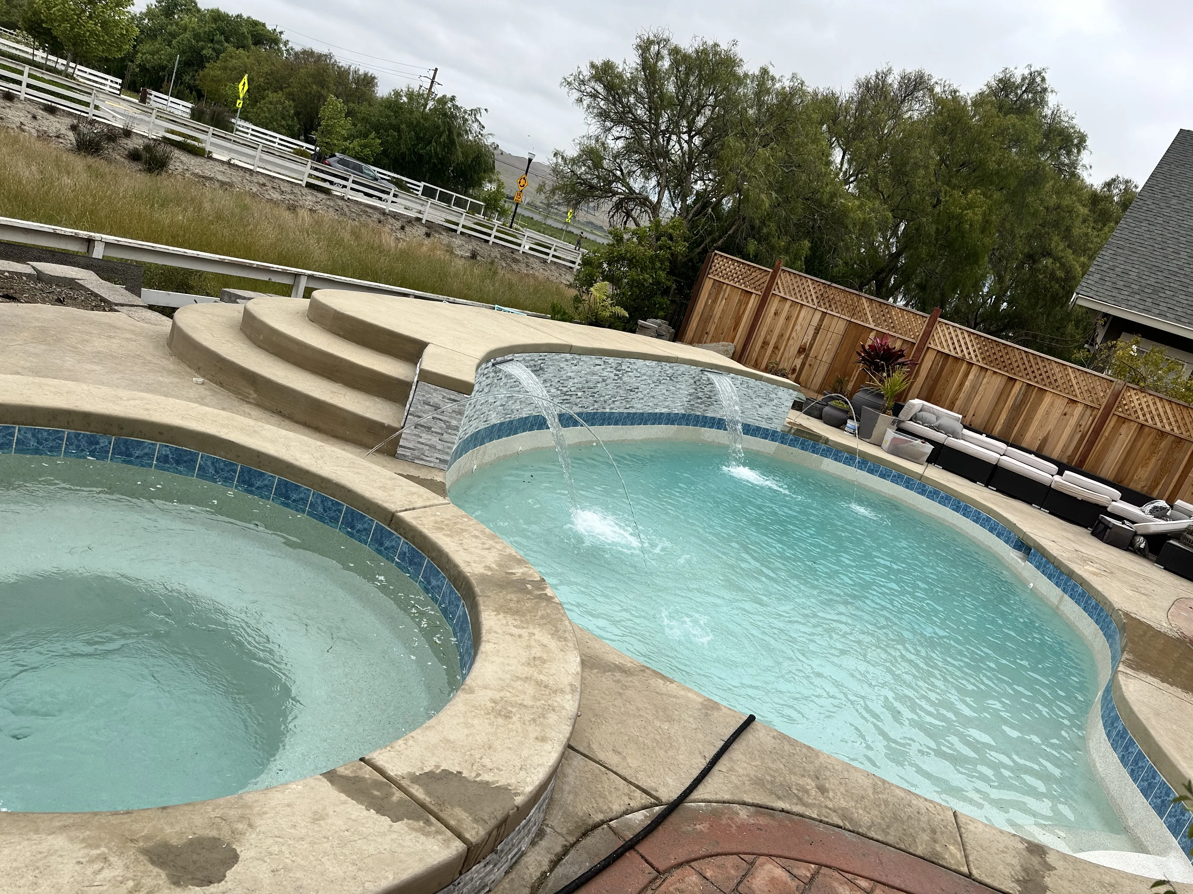 Finished freeform pool and elevated circular spa with spillover and water features surrounded by a concrete deck.