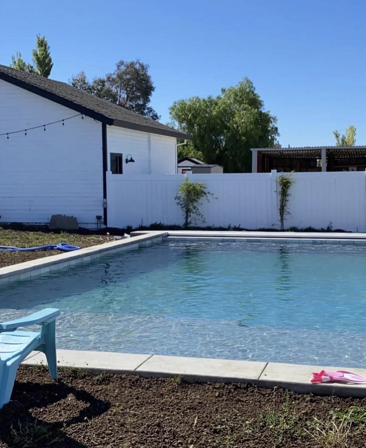 Finished rectangular pool with a baja shelf and concrete coping, surrounded by bare dirt in a residential backyard.