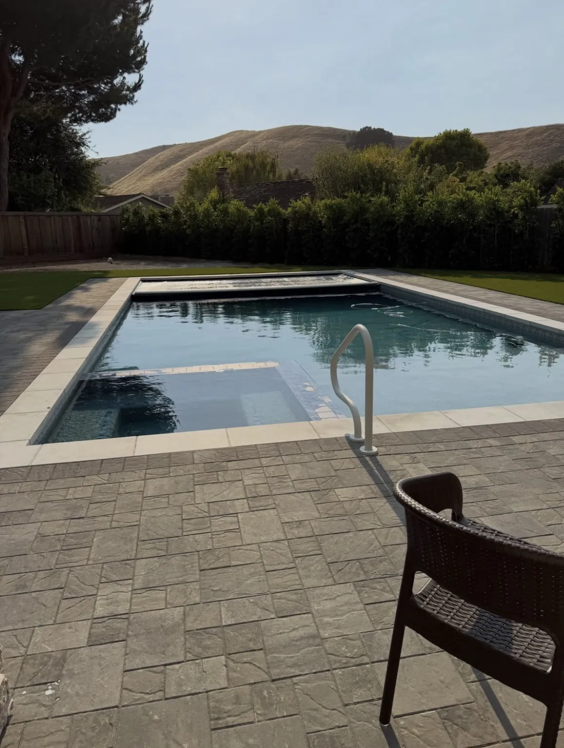Finished rectangular pool with a built-in spa, grey paver decking, and a partially retracted automatic cover.