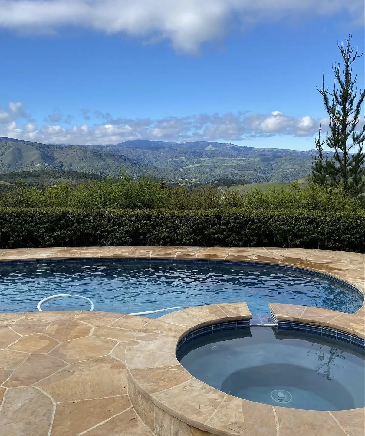 Finished freeform pool and raised spa with light brown flagstone deck overlooking a vast mountain landscape.