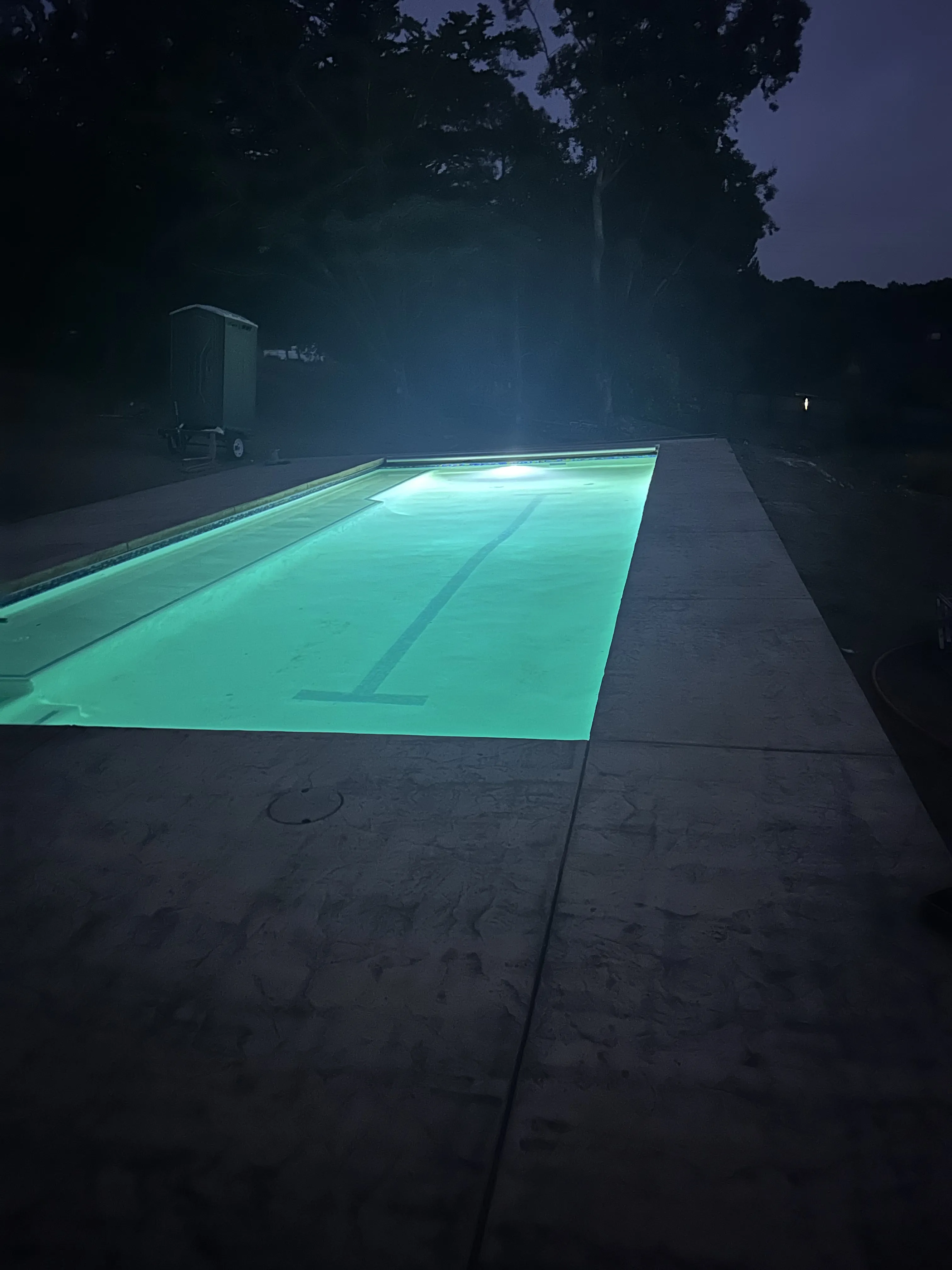 Finished rectangular lap pool brightly illuminated from within at night, surrounded by a concrete deck.