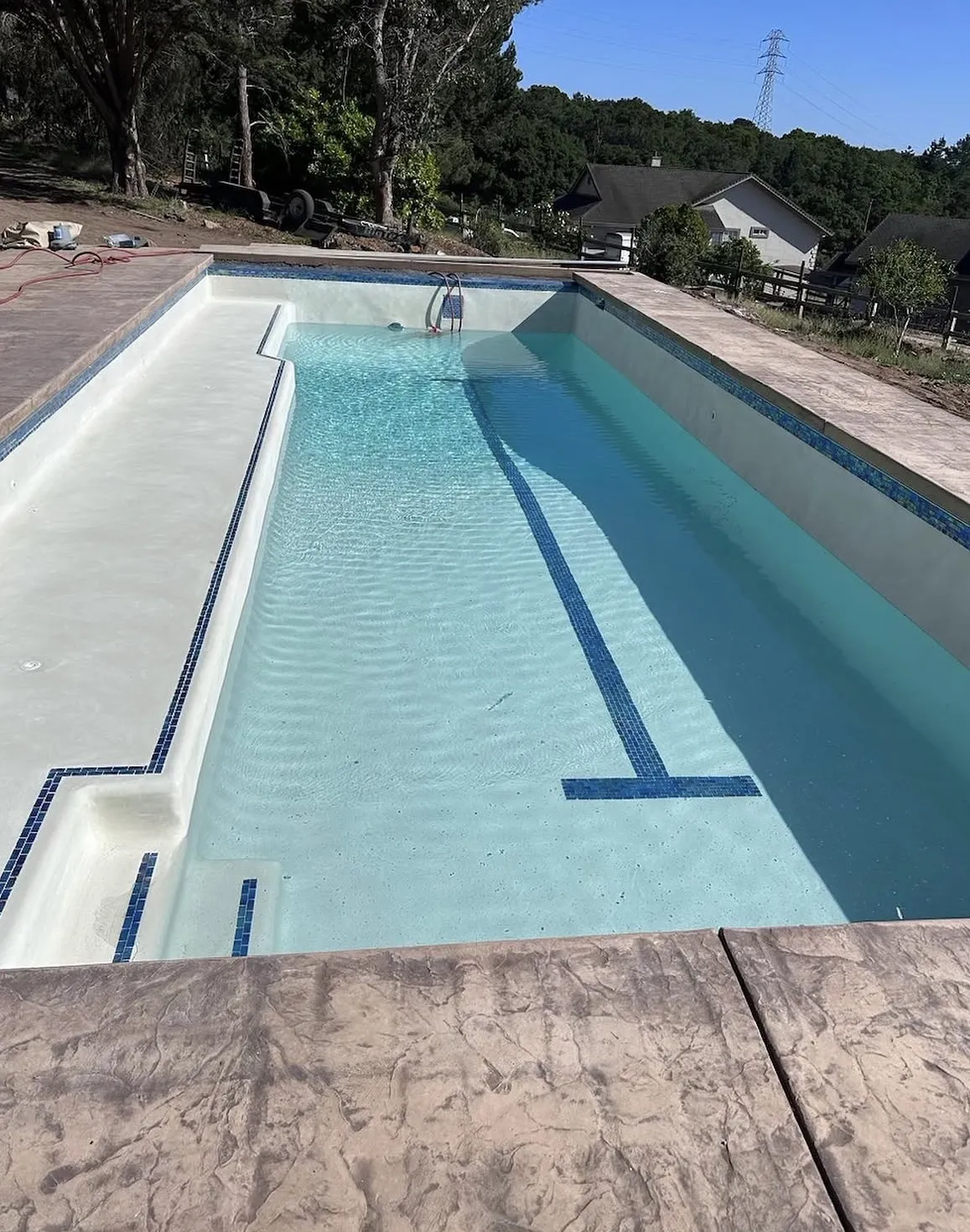 Rectangular lap pool filling with water featuring a blue tile lane marker and a side tanning ledge.