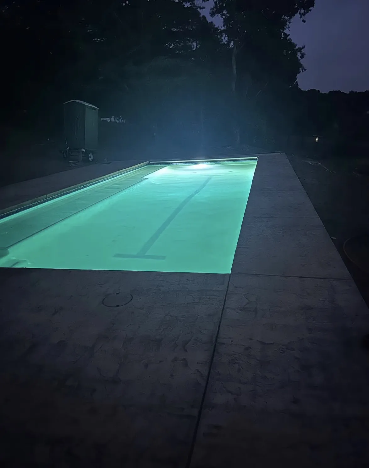 Illuminated rectangular pool at night featuring a dark lap lane marker and surrounded by a stamped concrete deck.