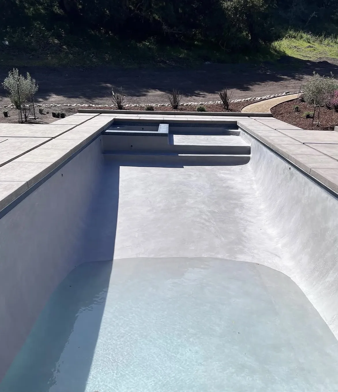 Newly plastered rectangular pool with integrated spa and concrete deck, partially filled with water.