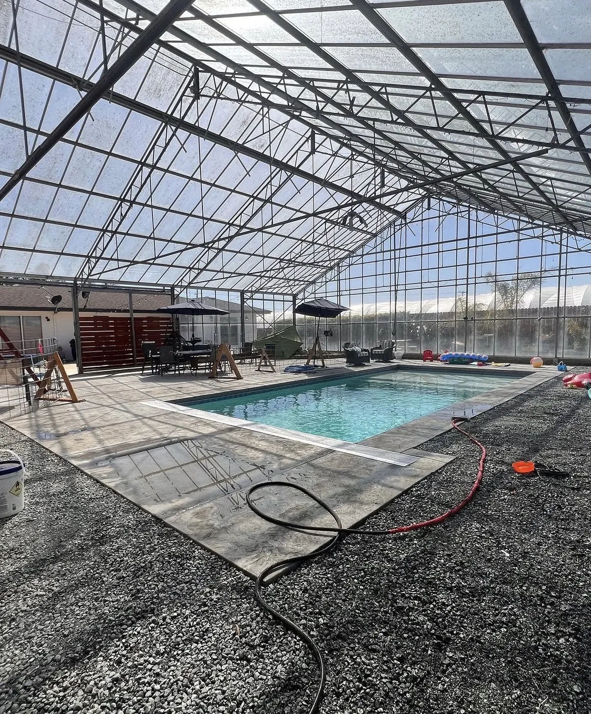 Finished rectangular swimming pool enclosed within a large glass and metal greenhouse structure.