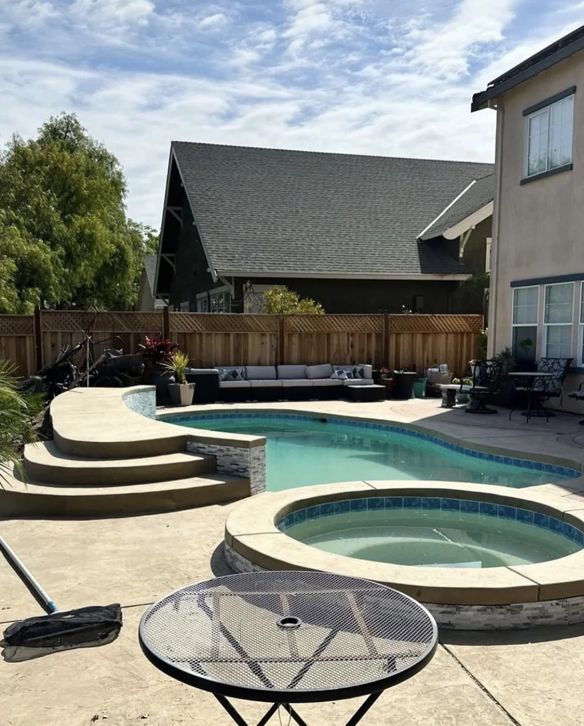 Completed freeform pool and raised circular spa with tiered concrete steps and a concrete deck.