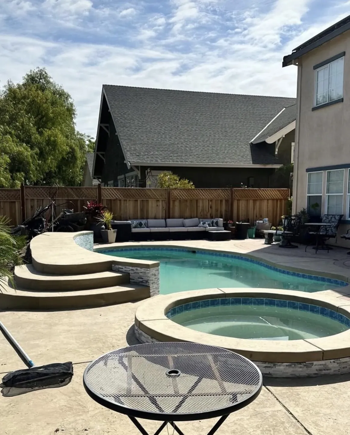 Completed freeform pool and raised circular spa with tiered concrete steps and a concrete deck.