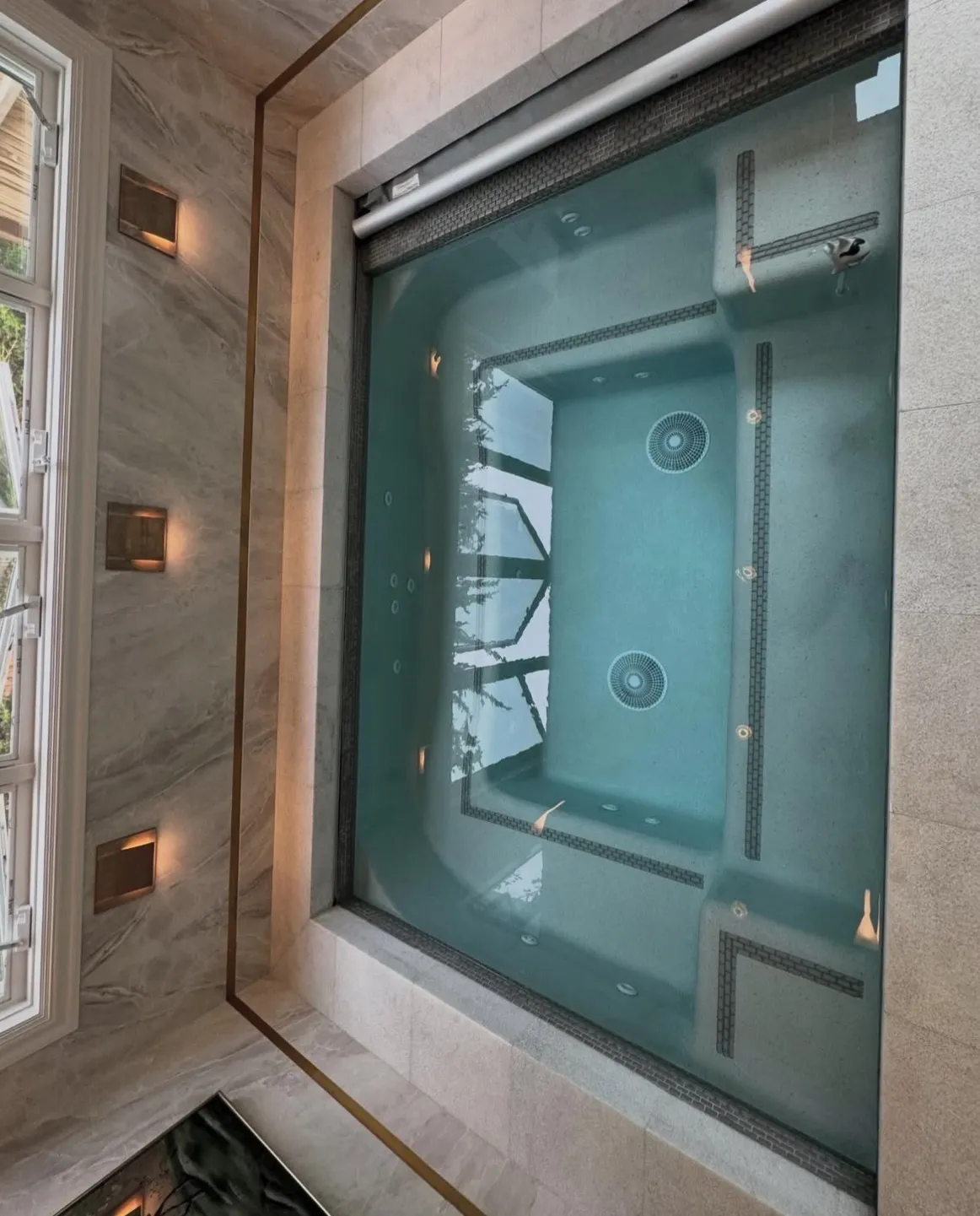 Steep overhead view of an indoor spa with teal finish, large-format stone surround, and a prominent reflection on the water.